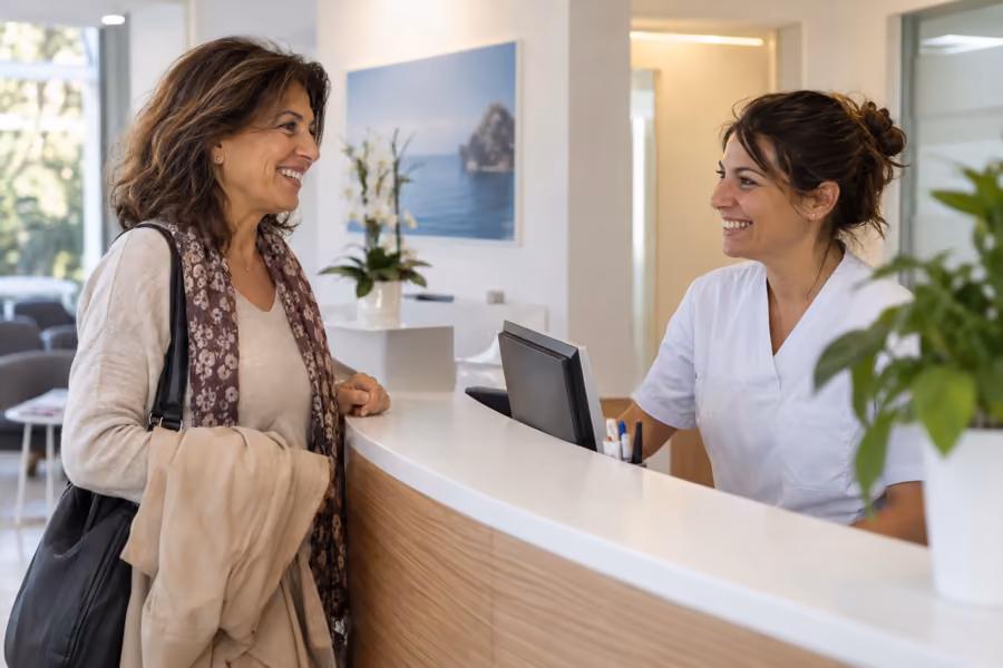 Una donna di mezza età viene accolta con un sorriso alla reception luminosa della clinica dentale per il controllo periodico.